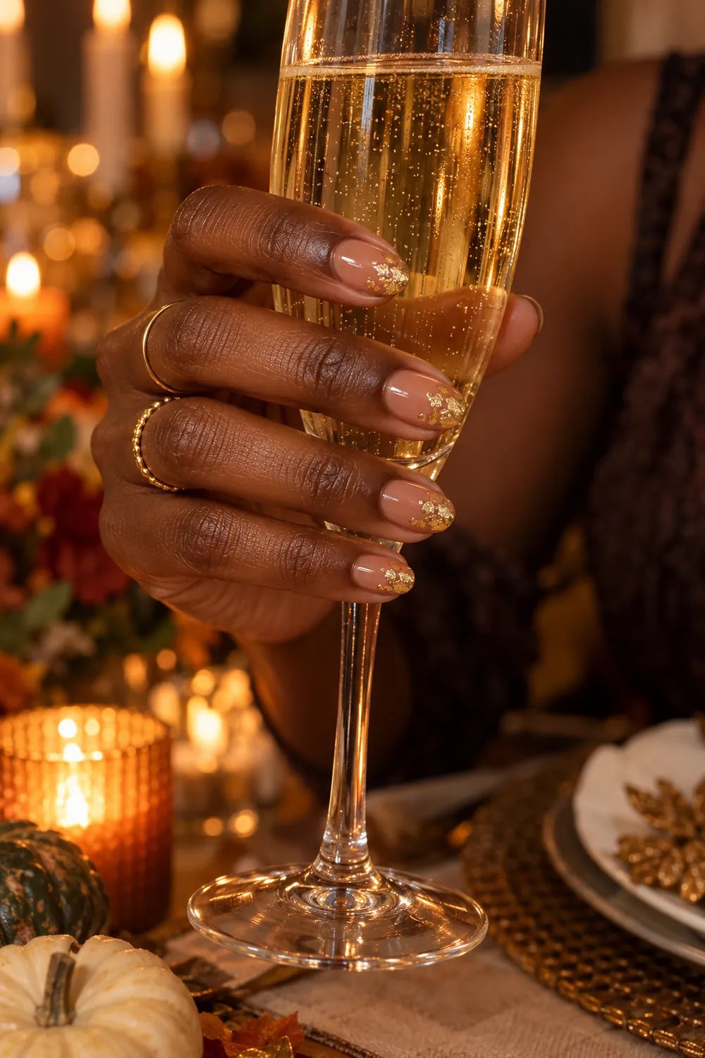 Short almond nude nails with gold leaf flakes holding a champagne glass